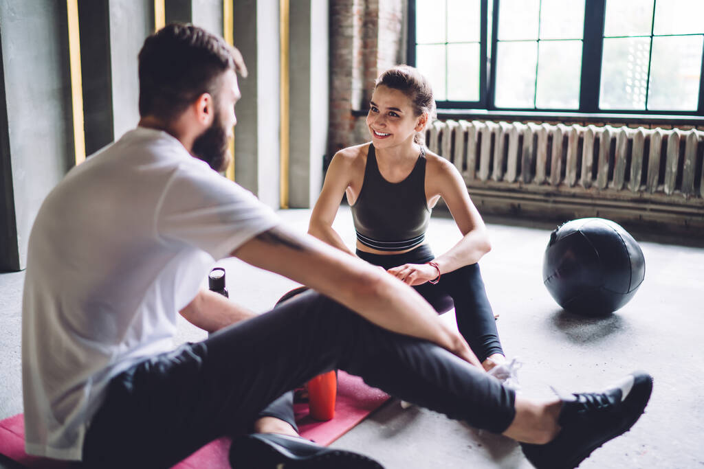 Mutlu genç 20 'li yaşlarda kadın spor salonunda erkek antrenörle konuşuyor danışmanlık üzerine egzersiz ve beslenme tartışıyorlar, egzersiz sonuçlarından memnun olan gülümseyen çift geri bildirimleri paylaşıyor - Fotoğraf, Görsel