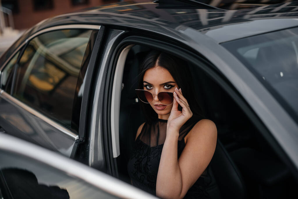 Stilvolles junges Mädchen in einem Business-Class-Auto in einem schwarzen Kleid. Business-Mode und -Stil - Foto, Bild