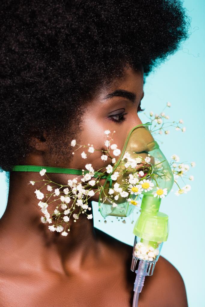 mujer joven afroamericana con flores en inhalador aislado sobre fondo azul - Foto, imagen