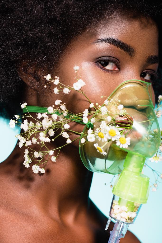 青い背景に隔離された吸入器の花を持つアフリカ系アメリカ人の若い女性 - 写真・画像