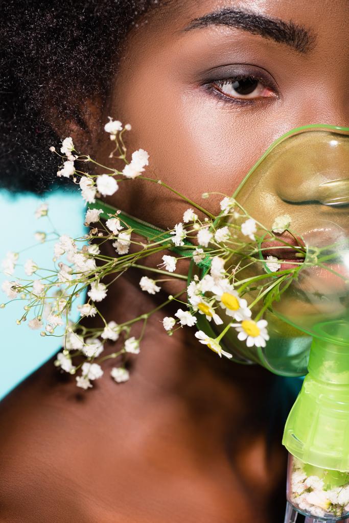 Mavi arka planda solunum cihazında çiçekleri olan Afrikalı Amerikalı genç bir kadının yakın çekimi. - Fotoğraf, Görsel