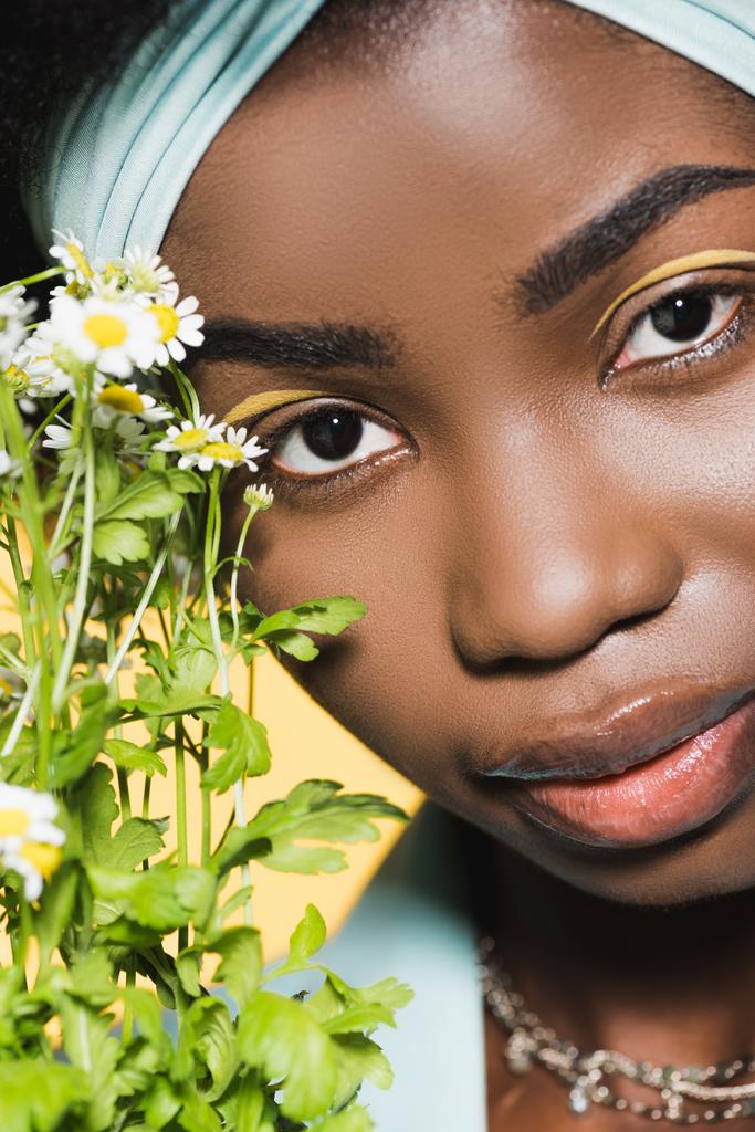 gros plan de jeune femme afro-américaine avec bouquet de camomille isolé sur jaune  - Photo, image