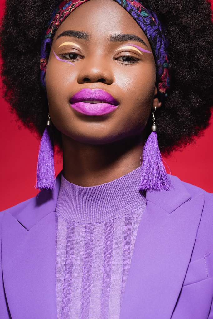 mujer joven afroamericana en traje elegante púrpura aislado en rojo - Foto, imagen