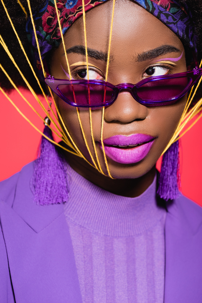アフリカ系アメリカ人の若い女性の紫のスタイリッシュな服とサングラス顔に黄色の文字列が赤に隔離された - 写真・画像