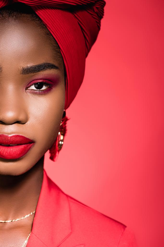 καλλιεργημένη άποψη της Αφροαμερικανής νεαρής γυναίκας με κομψό ντύσιμο και τουρμπάνι απομονώνονται σε κόκκινο - Φωτογραφία, εικόνα