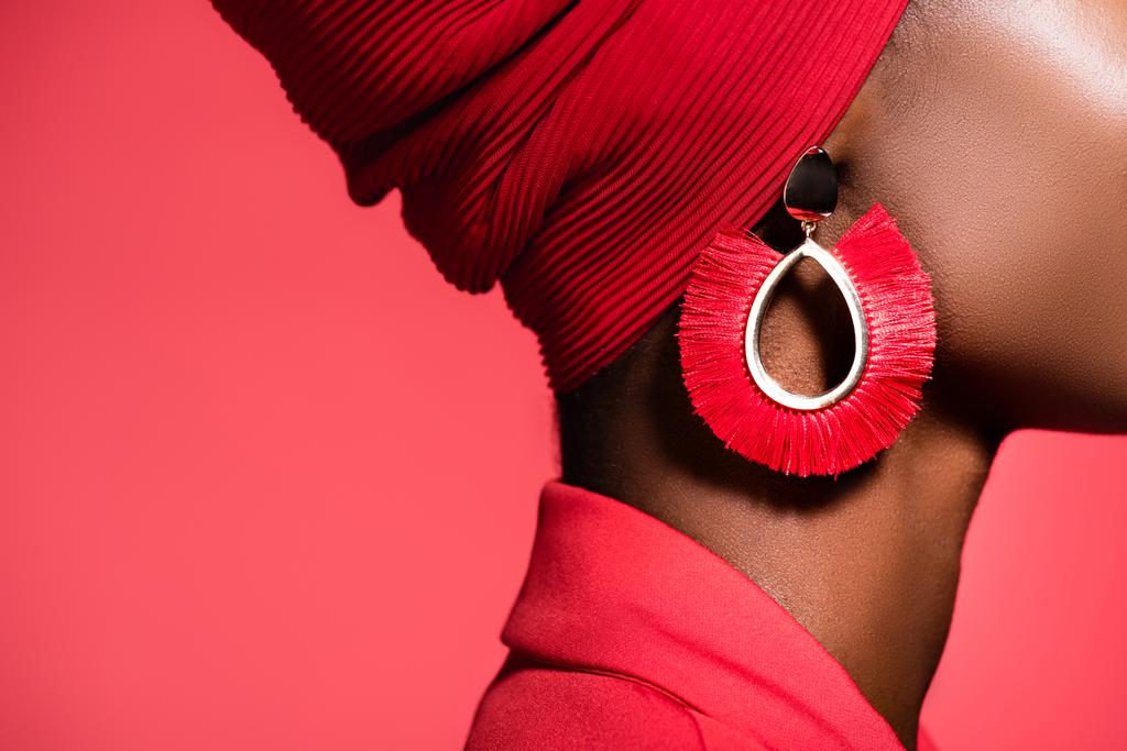 przycięty widok afrykańskiej młodej kobiety w stylowym kolczyku odizolowany na czerwono - Zdjęcie, obraz