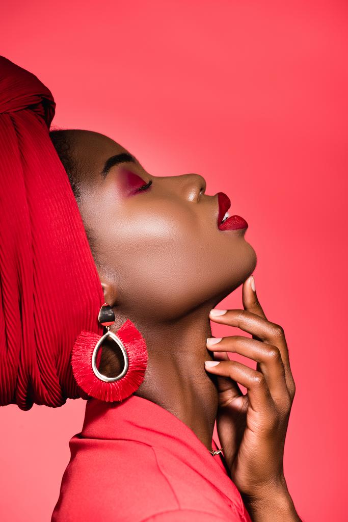 profile of african american young woman in stylish outfit and turban with closed eyes isolated on red - Photo, Image