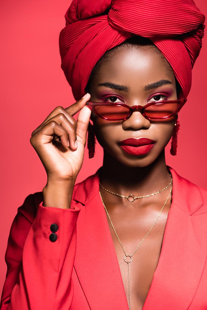 афро-американська молода жінка в стильному вбранні, сонцезахисні окуляри і турбан ізольовані на червоному
 - Фото, зображення