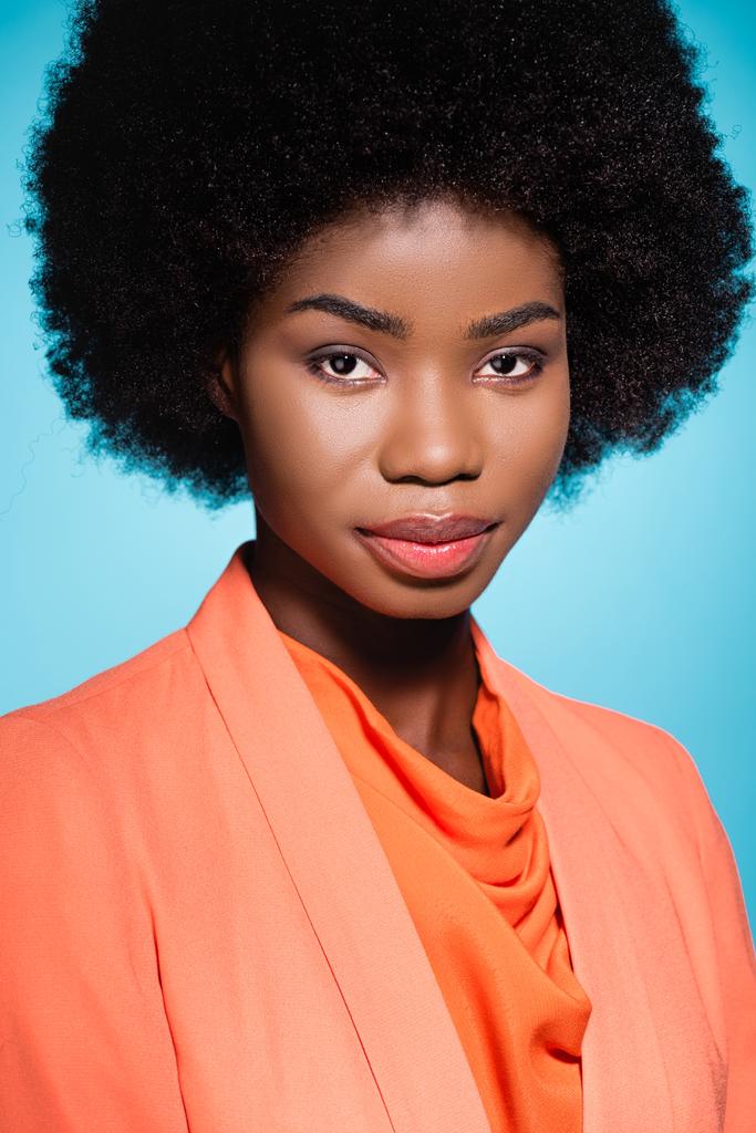 Afrikaans amerikaanse jonge vrouw in oranje stijlvolle outfit geïsoleerd op blauw - Foto, afbeelding