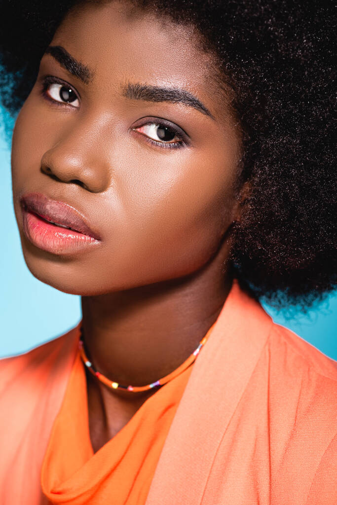 Afričanky americká mladá žena v oranžové stylové oblečení izolované na modré - Fotografie, Obrázek