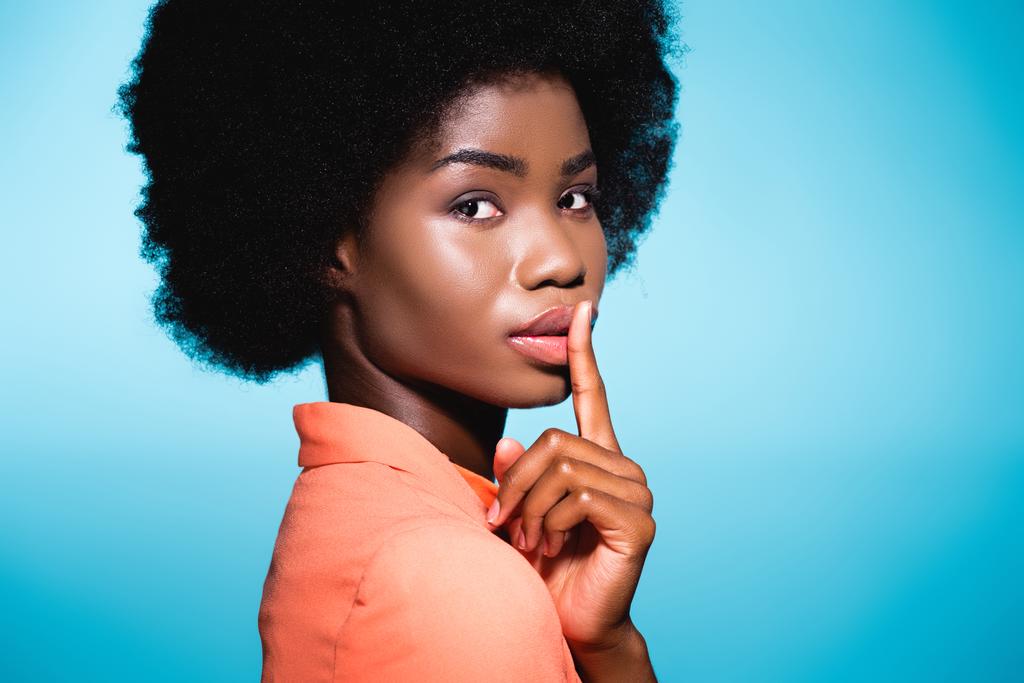 Afrikkalainen amerikkalainen nuori nainen oranssi tyylikäs asu osoittaa shh eristetty sininen - Valokuva, kuva