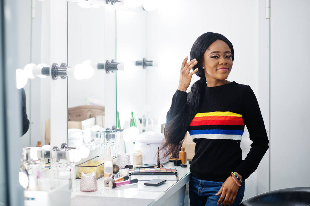 Portret van een Afro-Amerikaanse vrouw die make-up aanbrengt in een schoonheidssalon. - Foto, afbeelding