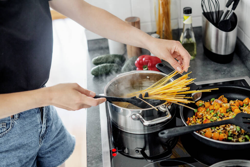 Junge Frau kocht zu Hause frische Spaghetti mit Gemüse. Gesundes veganes oder vegetarisches Konzept.  - Foto, Bild