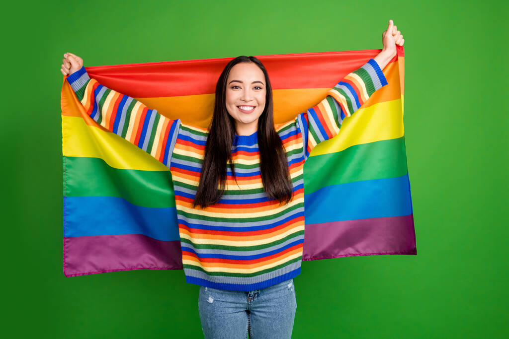 Portrait d'attrayant gai fille tenant dans les mains lgbt drapeau défilé isolé sur fond de couleur vert vif - Photo, image
