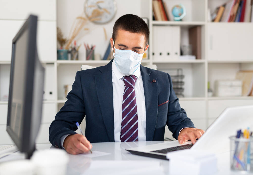 Сфокусированный бизнесмен в маске для лица работает в офисе - Фото, изображение