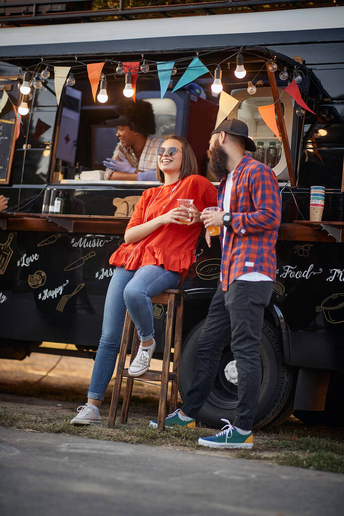 Junges urbanes kaukasisches Paar flirtet vor modifiziertem LKW für mobilen Fast-Food-Service - Foto, Bild