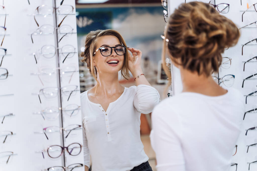 Κορίτσι στέκεται με το σύνολο των γυαλιών στο παρασκήνιο στο κατάστημα οπτικών. Σταθείτε με τα γυαλιά. Διόρθωση όρασης. Η γυναίκα φοράει γυαλιά.. - Φωτογραφία, εικόνα