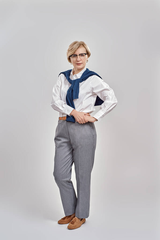 Full length shot of elegant middle aged caucasian woman wearing business attire and glasses looking at camera while posing, standing isolated over grey background - Foto, imagen