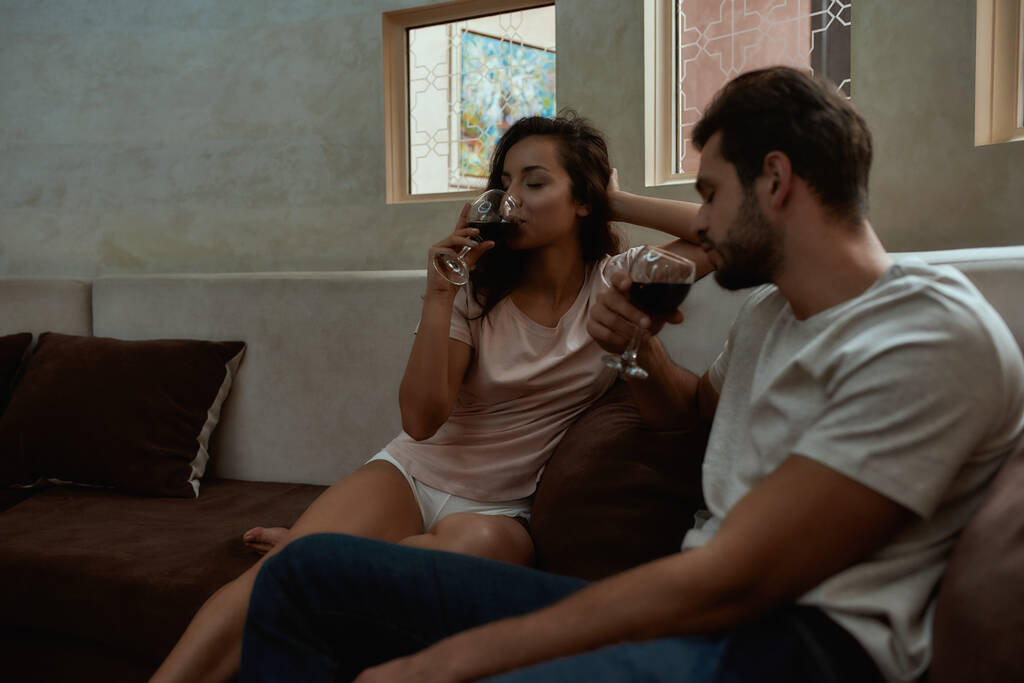 Zeit miteinander verbringen. Glückliches Paar entspannt sich und trinkt Wein, während es zu Hause auf der Couch sitzt - Foto, Bild