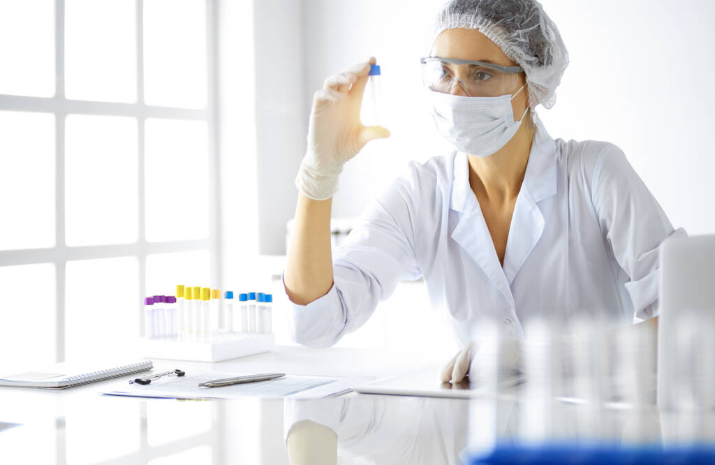 Professionista scienziata donna in occhiali protettivi tubo di ricerca con reagenti in laboratorio soleggiato. Medicina e ricerca - Foto, immagini