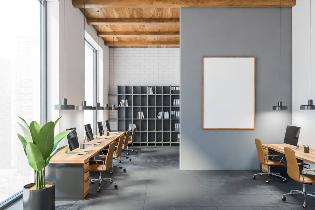 Cuarto de oficina gris y de madera con lienzo en blanco maqueta con computadoras en mesas y sillones de cuero marrón. Sala de negocios de espacio abierto con estanterías, pared y suelo gris, representación 3D sin personas - Foto, Imagen
