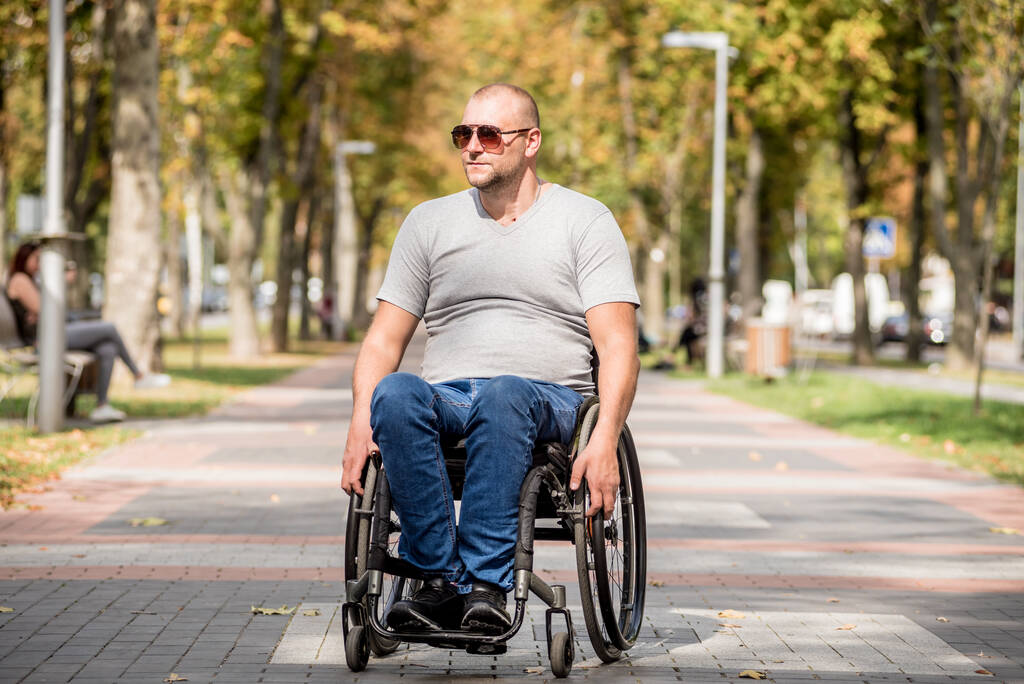 Mozgássérült férfi tolószékben sétál a park sikátorában. - Fotó, kép