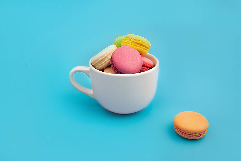 Macarons multicolores français dans une tasse de thé blanche. Dessert. - Photo, image