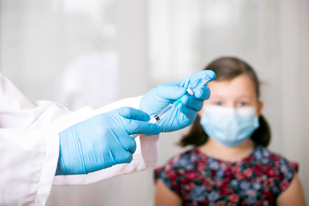 Дети прививают концепцию иммунизации. Врач вводит вакцину в руку маленькой девочки в маске для лица
. - Фото, изображение