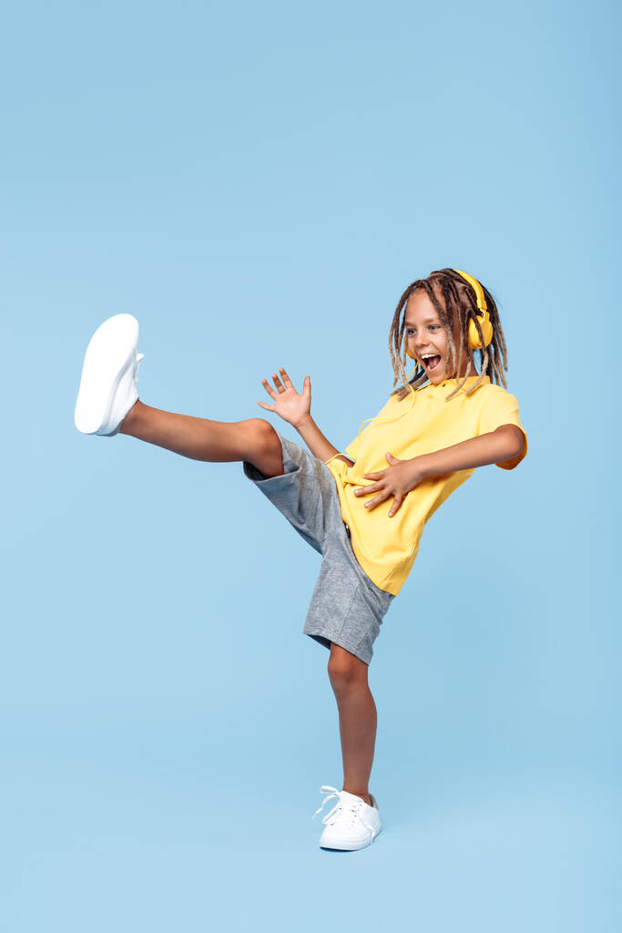 Gleeful little boy with african dreads listening music in headphones dancing over blue background. - Photo, Image