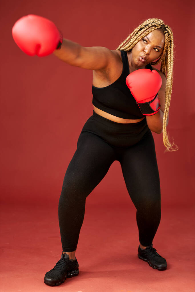 привлекательный молодой толстый черный спортивный боксер фитнес женщина в спортивной одежде разработка изолированы на красном фоне - Фото, изображение