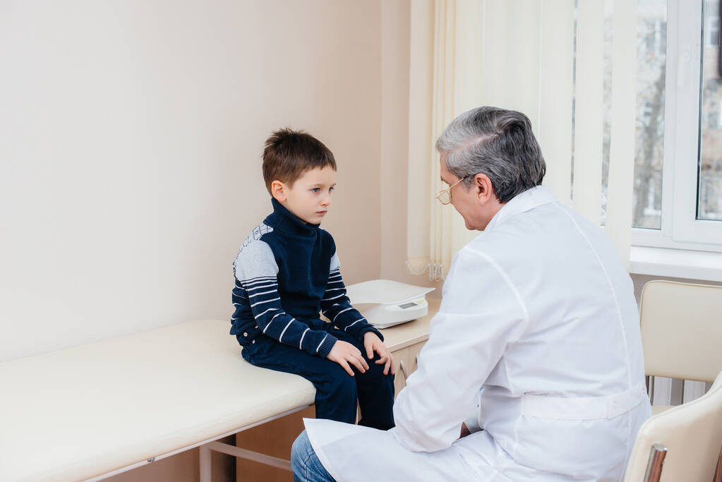 Een jonge jongen wordt beluisterd en behandeld door een ervaren arts in een moderne kliniek. Een virus en een epidemie. - Foto, afbeelding