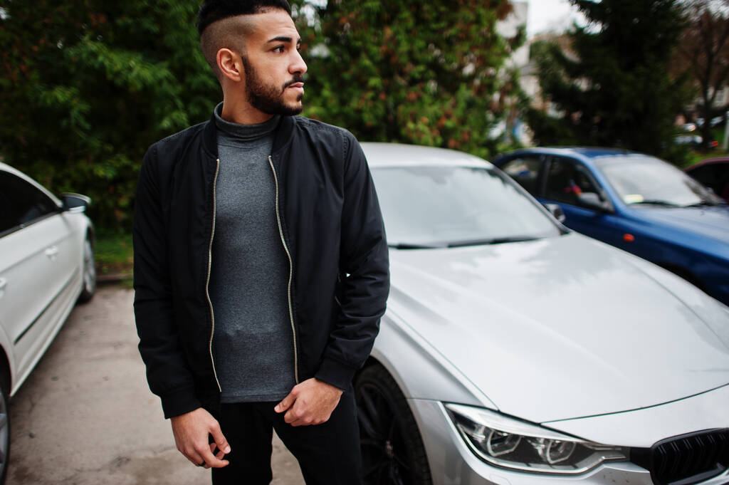 Portret van stijlvolle arabische baard man dragen grijze coltrui en zwarte jaket. Arabisch model man staan in de buurt van zijn auto. - Foto, afbeelding