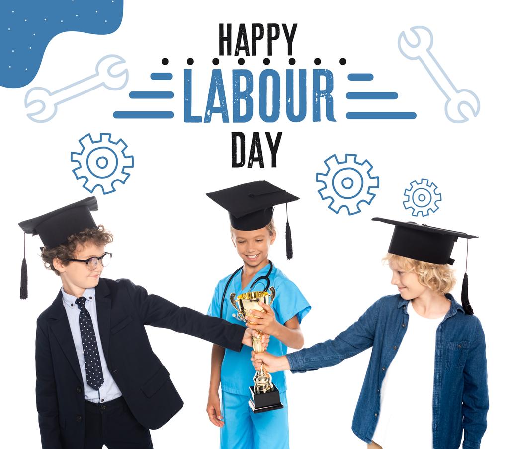 kids in graduation caps dressed in costumes of different professions holding golden trophy near happy labour day lettering on white  - Photo, Image