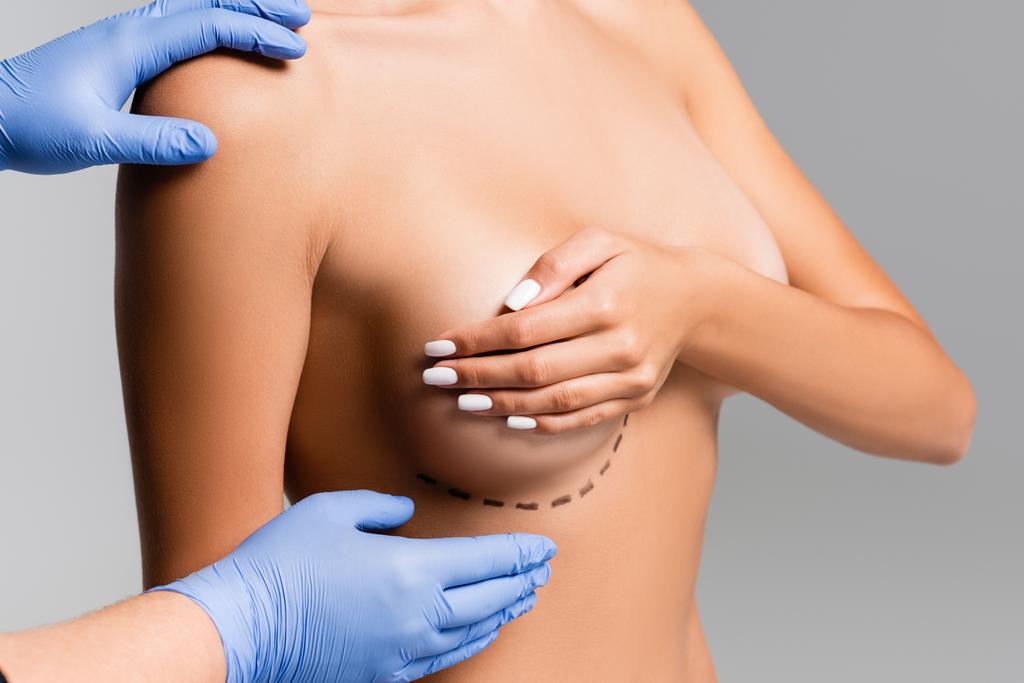 Vista recortada del cirujano plástico tocando mujer desnuda con líneas en el pecho aisladas en gris  - Foto, Imagen
