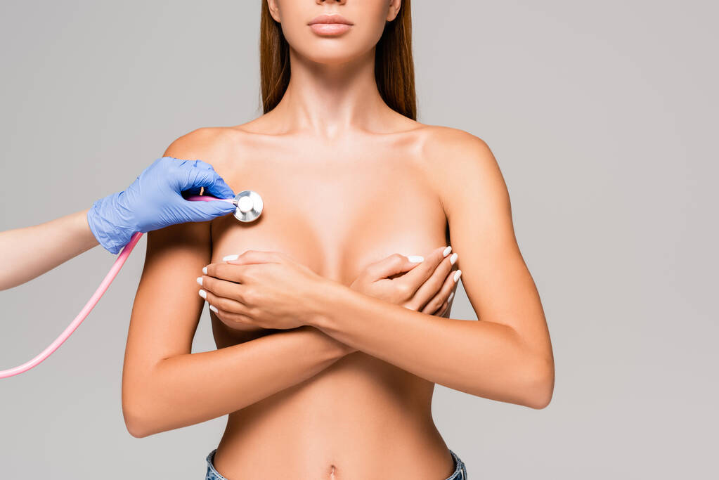 Oříznutý pohled na lékaře držícího stetoskop v blízkosti busty nahé ženy izolované na šedé  - Fotografie, Obrázek
