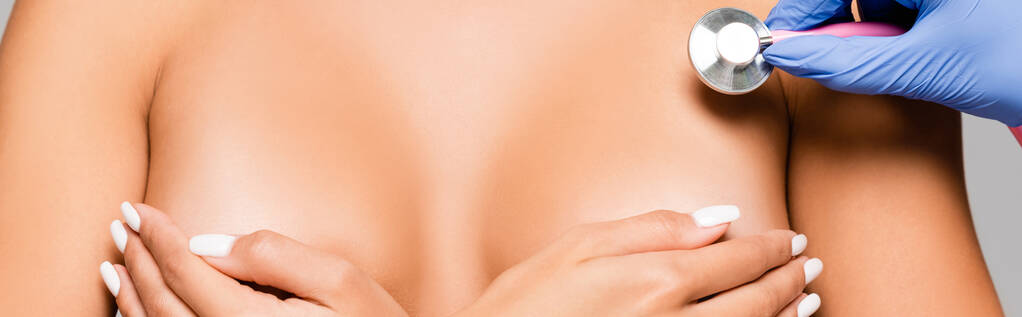 Vista cortada do médico em luva de látex segurando estetoscópio perto do peito de mulher nua isolada em cinza, banner  - Foto, Imagem