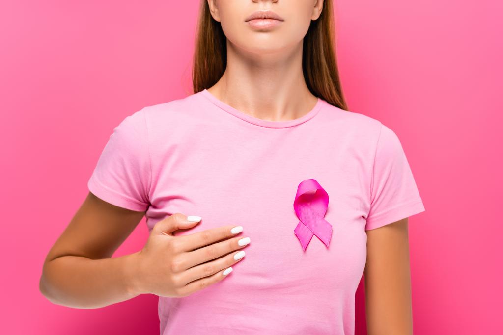 Cropped view of young woman with breast cancer awareness ribbon touching breast on pink background  - Photo, Image