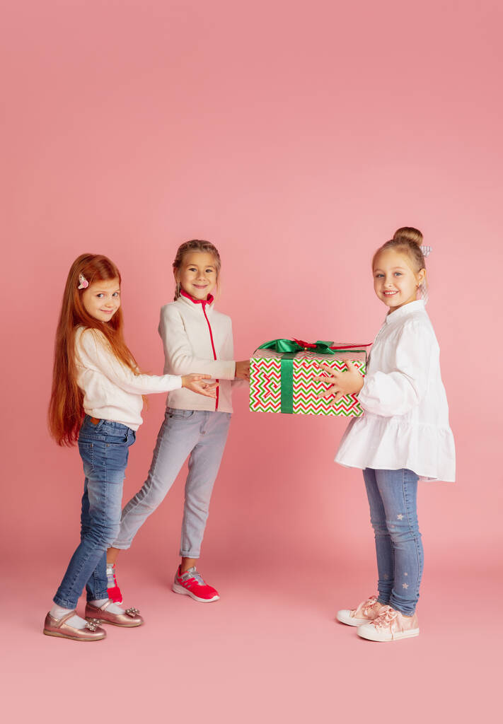 Noel tatilinde hediye vermek ve almak. Mutlu gülümseyen bir grup çocuk pembe stüdyo arka planında izole edilmiş eğleniyor. - Fotoğraf, Görsel