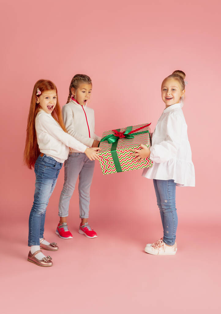 Dávat a dostávat dárky o vánočních svátcích. Skupina šťastně se usmívající děti baví izolované na růžovém pozadí studia - Fotografie, Obrázek