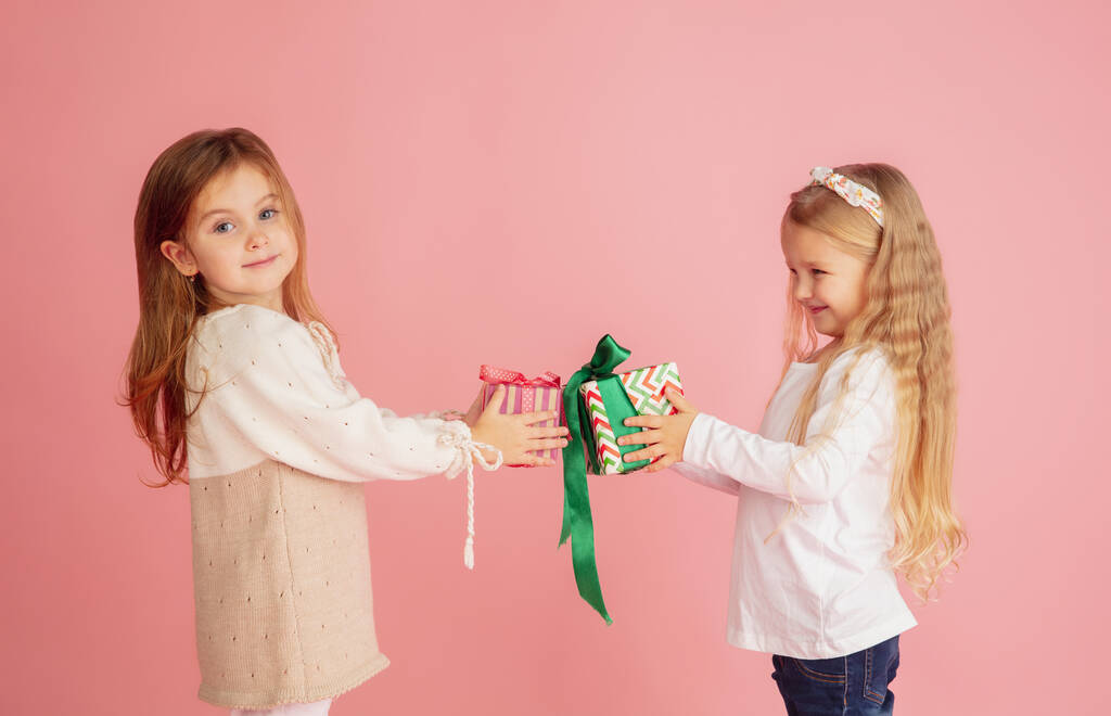 Dawanie i kupowanie prezentów na święta. Dwoje uśmiechniętych dzieci bawiących się wyizolowanych na różowym tle studia - Zdjęcie, obraz