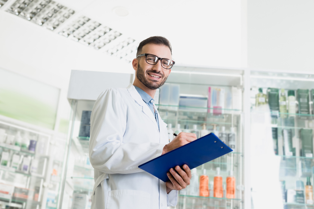 веселий фармацевт в окулярах і білому пальто, що пише на кишені в аптеці
  - Фото, зображення