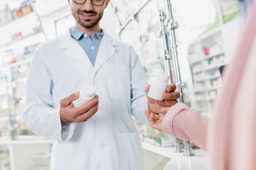levágott nézet gyógyszerész ad üveg tablettát az ügyfél a gyógyszertárban - Fotó, kép