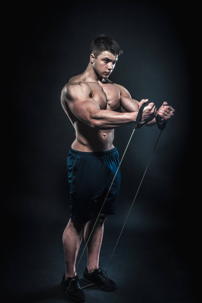 Σέξι νεαρός αθλητής που ποζάρει σε μαύρο φόντο στο Στούντιο. Γυμναστήριο, bodybuilding - Φωτογραφία, εικόνα
