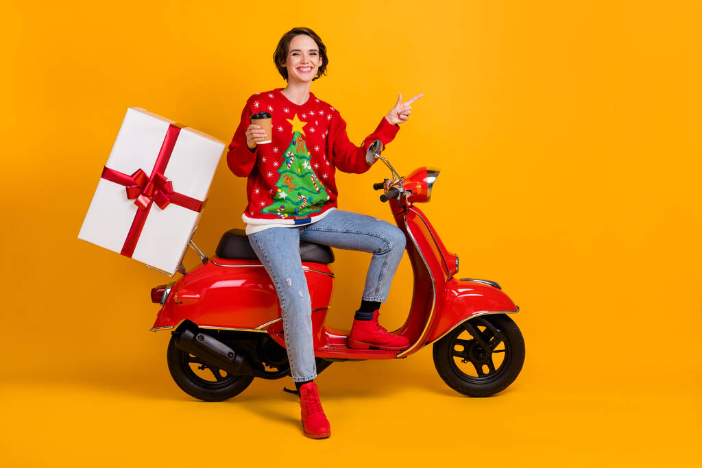 Full body photo of girl in christmas tree decor sweater jumper x-mas drive scooter break hold takeaway cup point finger copyspace isolated over yellow bright color background - Photo, Image