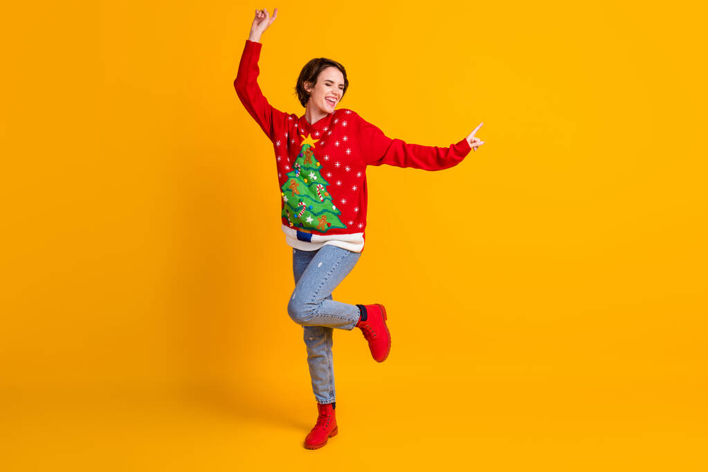 Pleine taille photo de fille gaie positive danse x-mas Nouvel An fête porter arbre de Noël décor pull bottes denim isolé sur fond de couleur jaune brillant - Photo, image