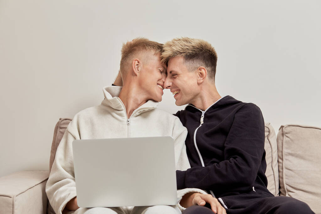 Két cuki férfi szerető otthon ül pizsamában. Laptop az ölemben.. - Fotó, kép