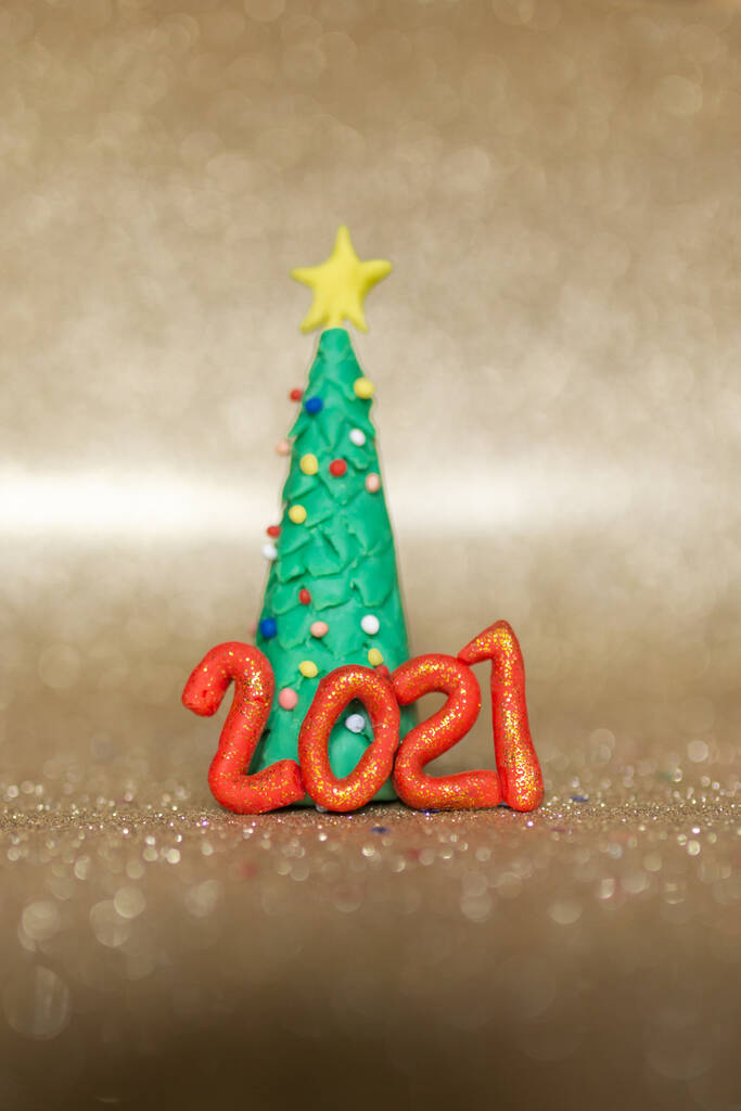 Spielerisches Weihnachtskonzept aus Ton. Bunte handgefertigte Miniatur-Weihnachtsbaum und Geschenke in Gold Hintergrund. Neues Jahr 2021. - Foto, Bild
