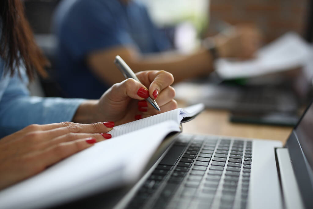 Mãos femininas segurar caneta e diário ao lado do laptop na mesa de trabalho. - Foto, Imagem