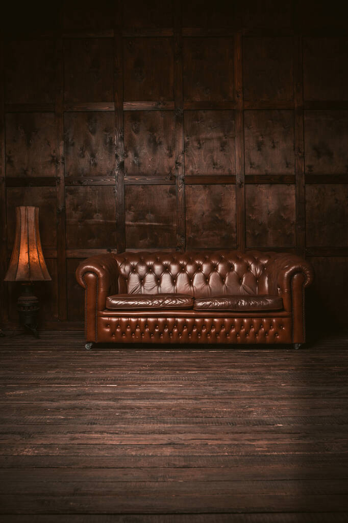  Sofá Chester de cuero en el interior de la habitación de madera con una vieja lámpara de pie. Imagen teñida de marrón - Foto, imagen