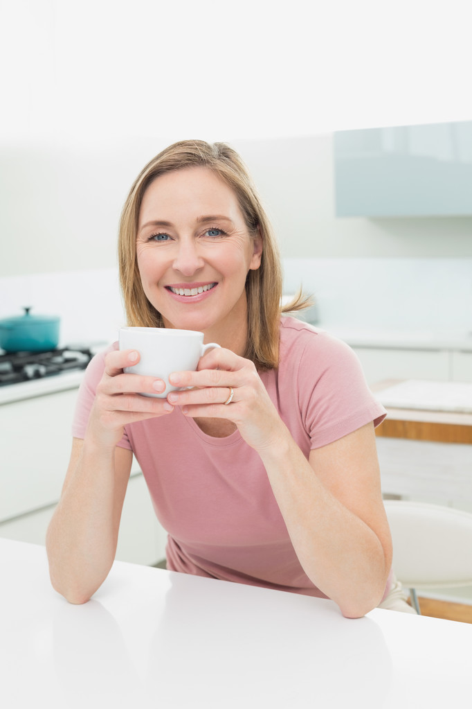 uvolněné usmívající se žena s kávou v kuchyni - Fotografie, Obrázek